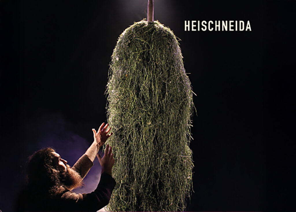 Ein Vollbartiger Mann steht vor viel Heu und hat die Haltung als würde er es anbeten