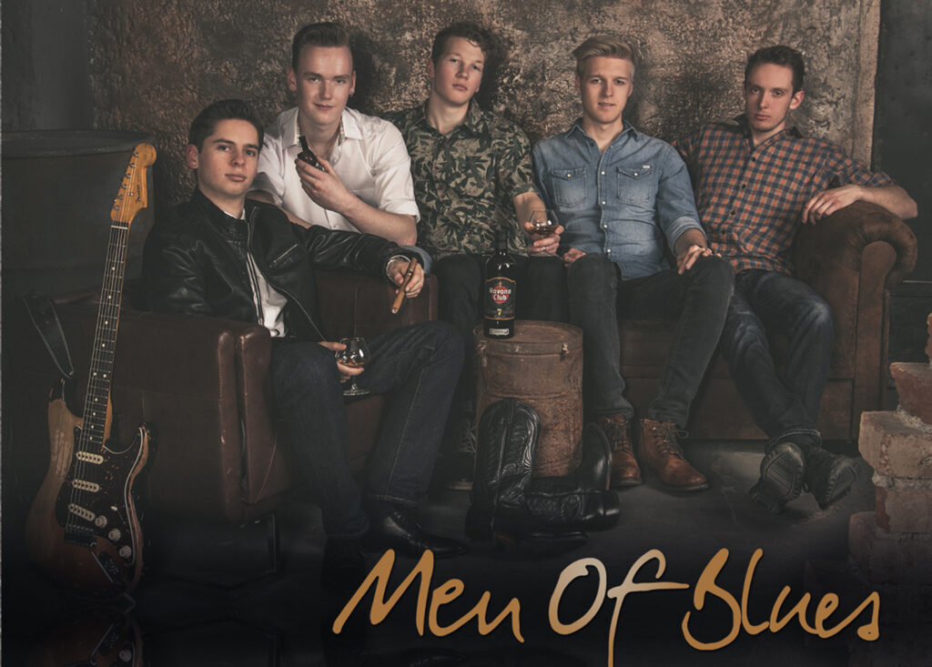 5 Junge Musiker sitzen auf einer braunen Ledercouch, mit Zigarre und braunem Rum. Eine Gitarre lehnt an dem Sofa.